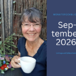 Ulrike Wanner, lächelnd mit Brille und grauem Haar, hält im Garten eine weiße Tasse, daneben ein bunter Blumenstrauß auf dem Tisch.