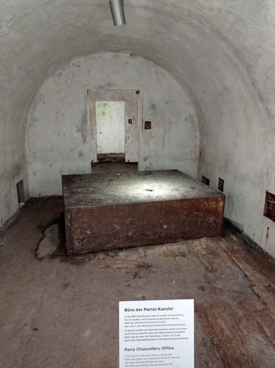 Großer rostiger Panzerschrank in der Mitte eines gewölbten Bunkerraums, davor eine Tafel zum Büro der Partei-Kanzlei