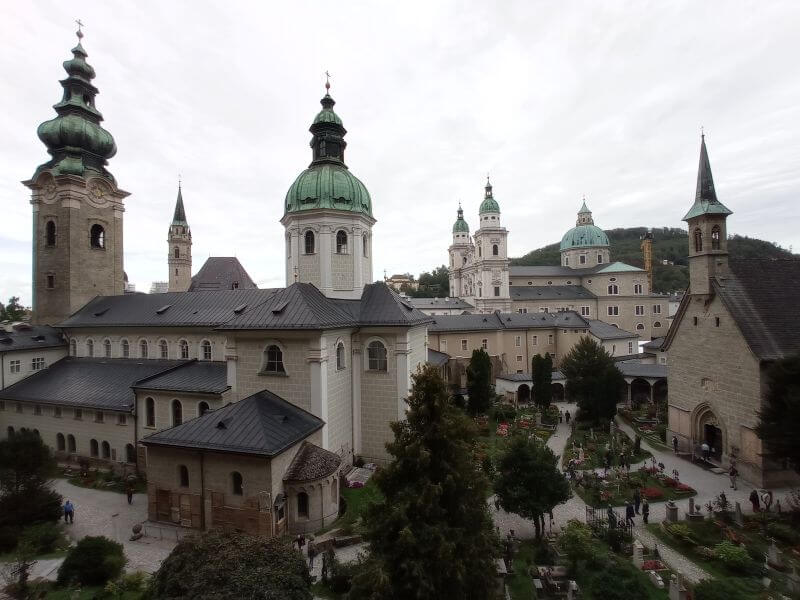 Blick von oben über den Petersfriedhof auf die grünen Kuppeln und Türme von Stift St. Peter, dahinter der Dom